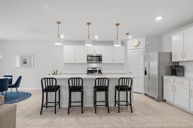 kitchen with appliances with stainless steel finishes, a kitchen island with sink, white cabinets, and decorative light fixtures