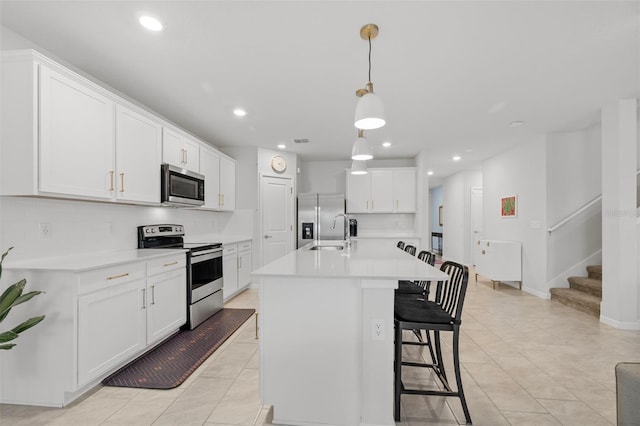 kitchen featuring pendant lighting, decorative backsplash, white cabinetry, an island with sink, and stainless steel appliances