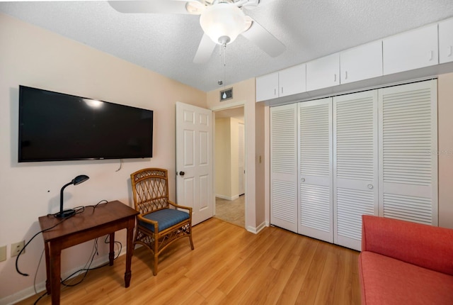 living area with light wood-type flooring, ceiling fan, and a textured ceiling