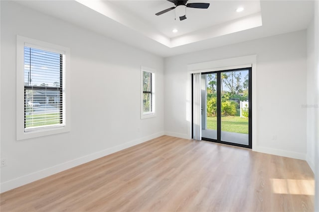 unfurnished room with ceiling fan, a healthy amount of sunlight, light wood-type flooring, and a tray ceiling