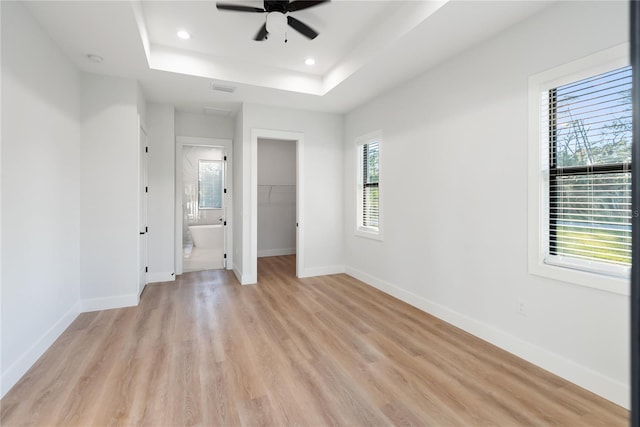 unfurnished bedroom with a spacious closet, ensuite bath, a closet, ceiling fan, and a tray ceiling