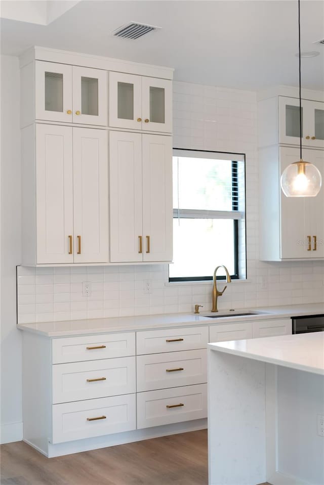 kitchen featuring backsplash, light wood-type flooring, hanging light fixtures, white cabinets, and sink