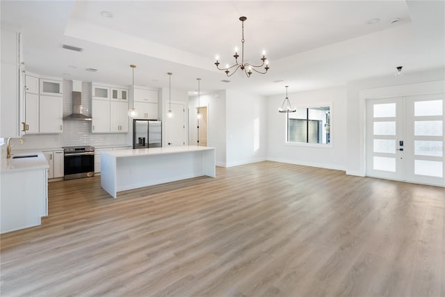 kitchen featuring wall chimney range hood, a kitchen island, a raised ceiling, appliances with stainless steel finishes, and white cabinets