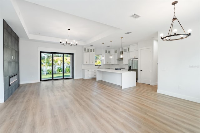 kitchen with white cabinets, a kitchen island, decorative light fixtures, an inviting chandelier, and a raised ceiling