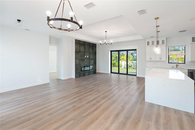 unfurnished living room with a chandelier, light hardwood / wood-style flooring, a tray ceiling, and sink