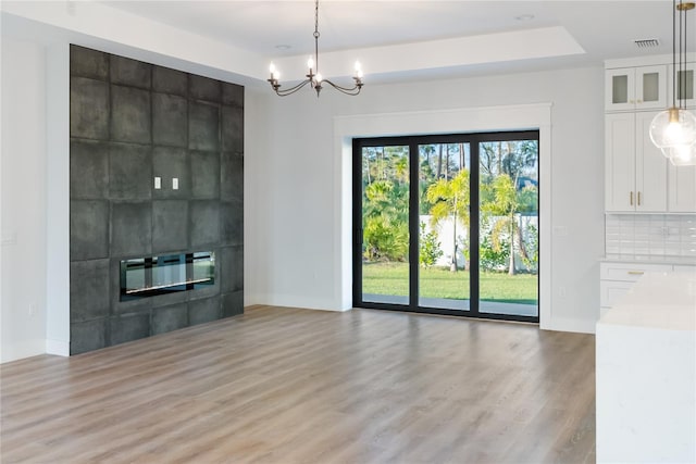 unfurnished living room with an inviting chandelier, a tile fireplace, light hardwood / wood-style flooring, and a tray ceiling