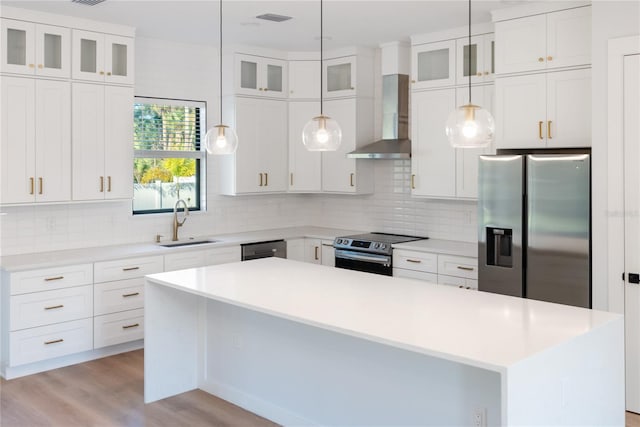 kitchen with stainless steel appliances, wall chimney range hood, a kitchen island, white cabinets, and sink