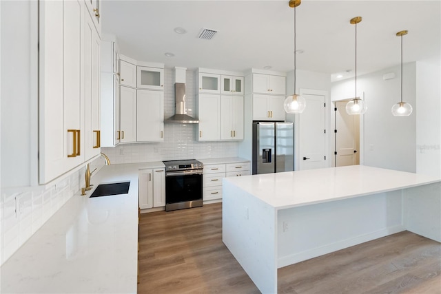 kitchen featuring white cabinets, wall chimney exhaust hood, stainless steel appliances, sink, and hanging light fixtures