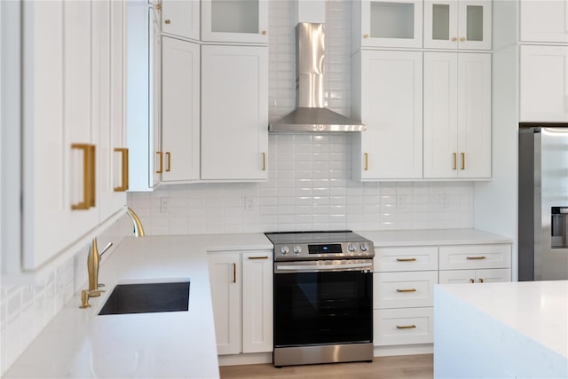 kitchen featuring sink, wall chimney range hood, stainless steel appliances, and white cabinetry