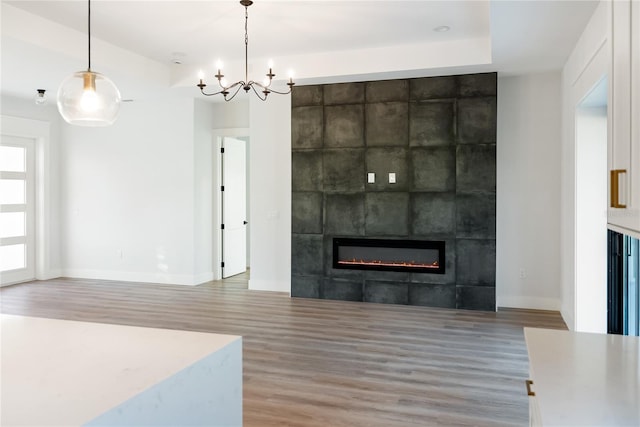 unfurnished living room featuring wood-type flooring, a tile fireplace, and an inviting chandelier