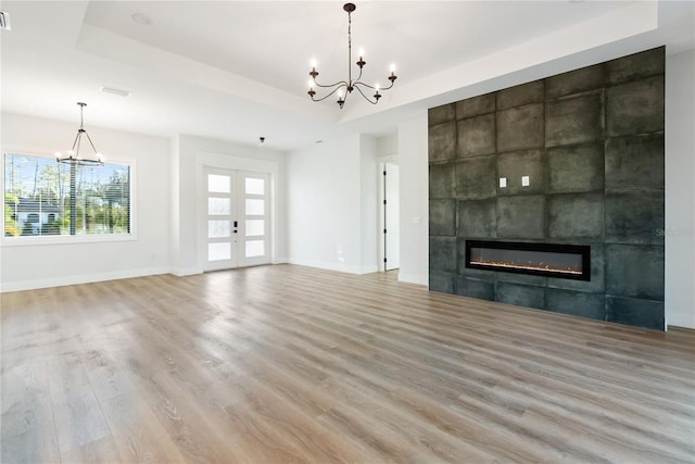 unfurnished living room featuring french doors, a notable chandelier, hardwood / wood-style flooring, a tray ceiling, and a tiled fireplace