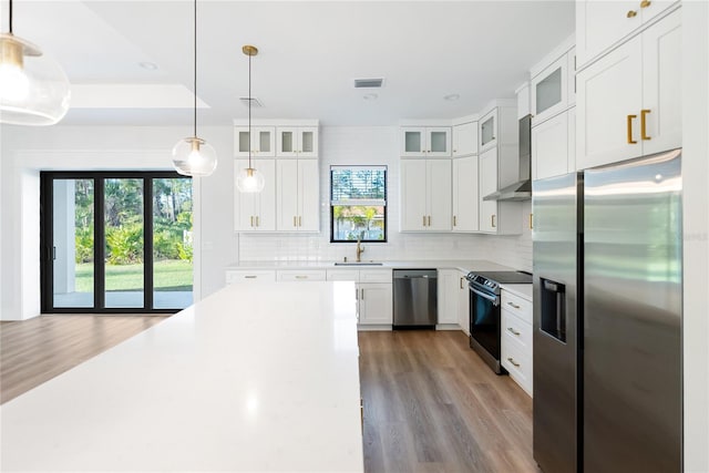 kitchen featuring stainless steel appliances, tasteful backsplash, hanging light fixtures, wall chimney range hood, and white cabinets