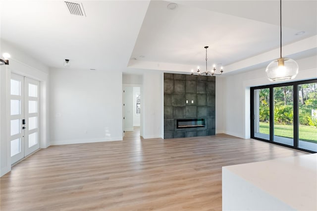 unfurnished living room featuring light wood-type flooring, a chandelier, a fireplace, and a raised ceiling