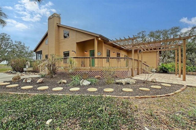 rear view of property featuring a pergola, a wooden deck, and a patio