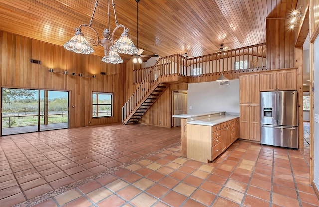 kitchen with wood walls, kitchen peninsula, stainless steel refrigerator with ice dispenser, decorative light fixtures, and ceiling fan with notable chandelier