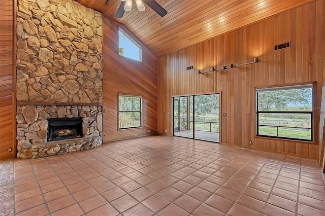 unfurnished living room featuring high vaulted ceiling, wood walls, a stone fireplace, and wood ceiling