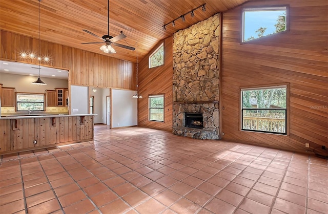 unfurnished living room featuring track lighting, wood ceiling, wooden walls, a fireplace, and high vaulted ceiling