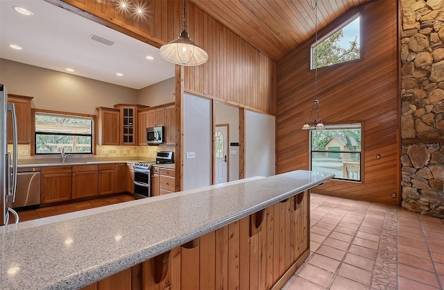 kitchen featuring stainless steel appliances, sink, hanging light fixtures, high vaulted ceiling, and light stone counters