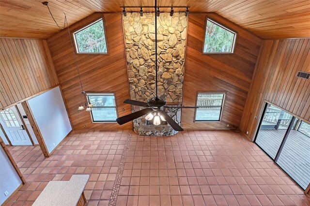 unfurnished living room with ceiling fan, a wealth of natural light, rail lighting, and wood walls