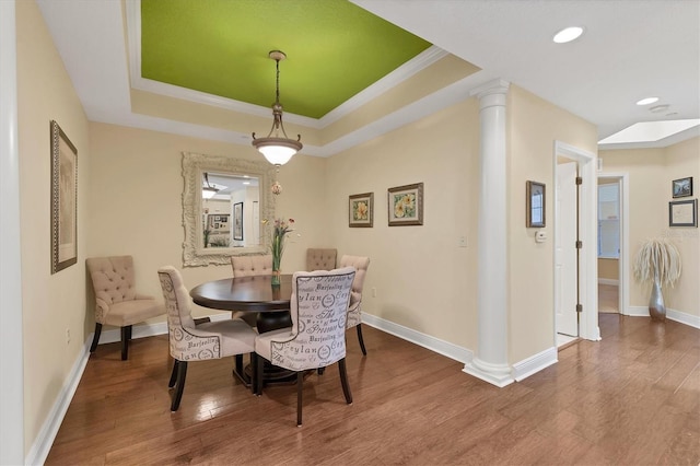 dining area with decorative columns, wood-type flooring, a tray ceiling, and ornamental molding