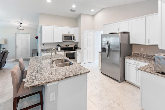 kitchen featuring a kitchen breakfast bar, a kitchen island with sink, appliances with stainless steel finishes, white cabinetry, and lofted ceiling