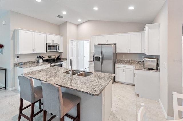 kitchen with vaulted ceiling, stainless steel appliances, a center island with sink, white cabinets, and sink