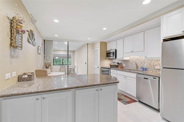 kitchen featuring backsplash, a peninsula, white cabinets, stainless steel appliances, and a sink