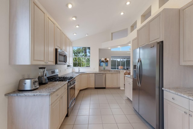 kitchen featuring lofted ceiling, sink, light stone countertops, appliances with stainless steel finishes, and light tile patterned floors