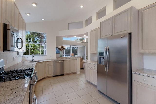 kitchen featuring sink, light tile patterned flooring, light stone countertops, appliances with stainless steel finishes, and high vaulted ceiling