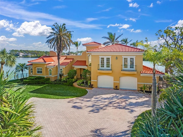 mediterranean / spanish home featuring a garage, a front lawn, and a water view