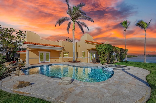 pool at dusk with a water view, french doors, an in ground hot tub, and a patio