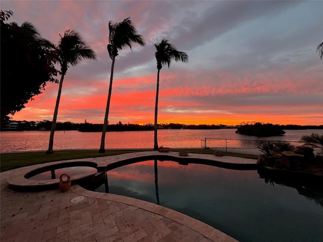 pool at dusk with a patio area and a water view