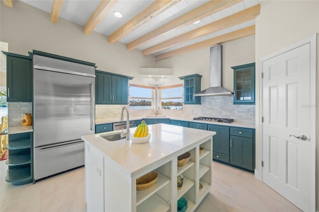 kitchen featuring beam ceiling, decorative backsplash, an island with sink, stainless steel appliances, and wall chimney exhaust hood