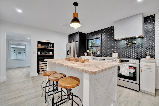 kitchen featuring stainless steel appliances, decorative light fixtures, white cabinetry, a center island, and wall chimney exhaust hood