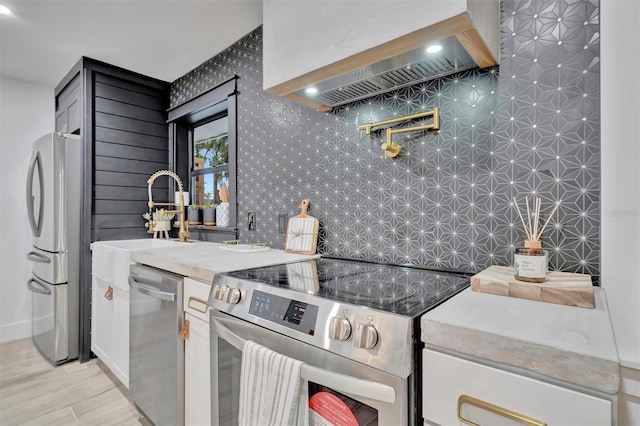 kitchen featuring sink, custom range hood, white cabinetry, and appliances with stainless steel finishes