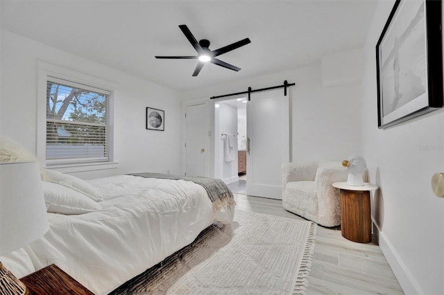 bedroom with ceiling fan, light hardwood / wood-style flooring, connected bathroom, and a barn door