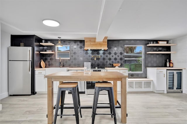 kitchen featuring white cabinets, refrigerator, stainless steel range, and wine cooler