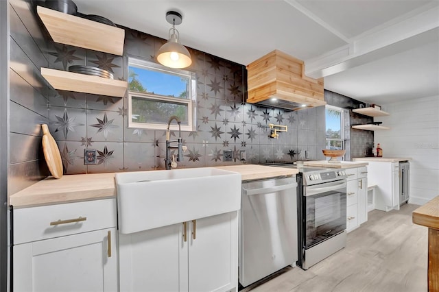 kitchen featuring stainless steel appliances, sink, white cabinets, butcher block counters, and hanging light fixtures