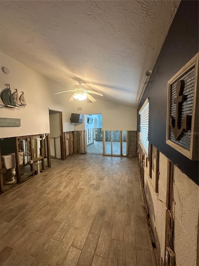 unfurnished living room featuring ceiling fan, wood-type flooring, a textured ceiling, and vaulted ceiling