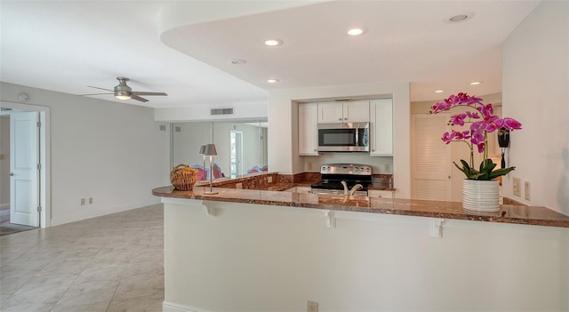 kitchen with kitchen peninsula, white cabinetry, appliances with stainless steel finishes, a breakfast bar area, and dark stone counters