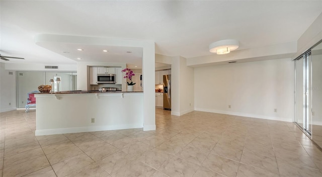 kitchen with white cabinets, appliances with stainless steel finishes, a kitchen bar, kitchen peninsula, and ceiling fan