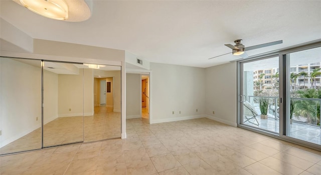 tiled spare room featuring ceiling fan and a wall of windows