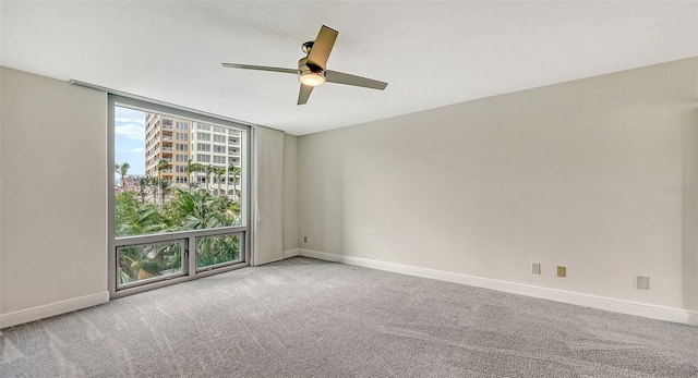 empty room with ceiling fan, light colored carpet, and a wall of windows