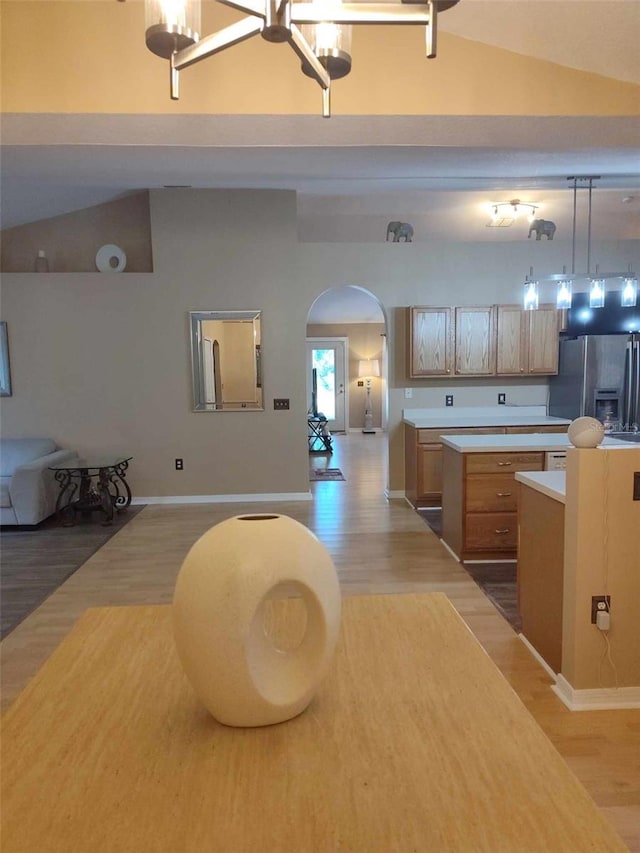 kitchen featuring decorative light fixtures, light wood-type flooring, stainless steel fridge, and vaulted ceiling