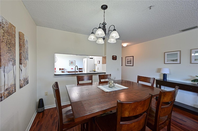 dining space featuring dark hardwood / wood-style floors, a chandelier, sink, and a textured ceiling