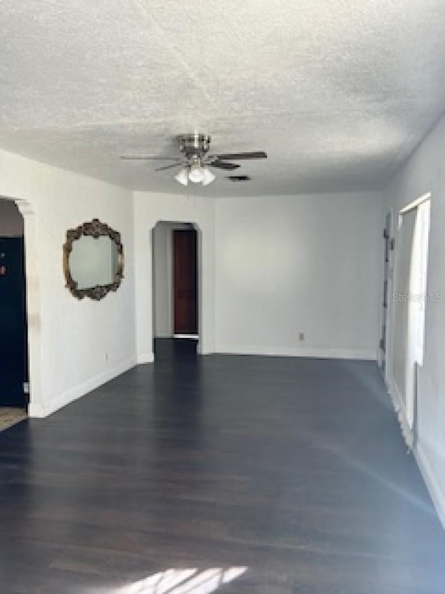 empty room with a textured ceiling, ceiling fan, and dark wood-type flooring