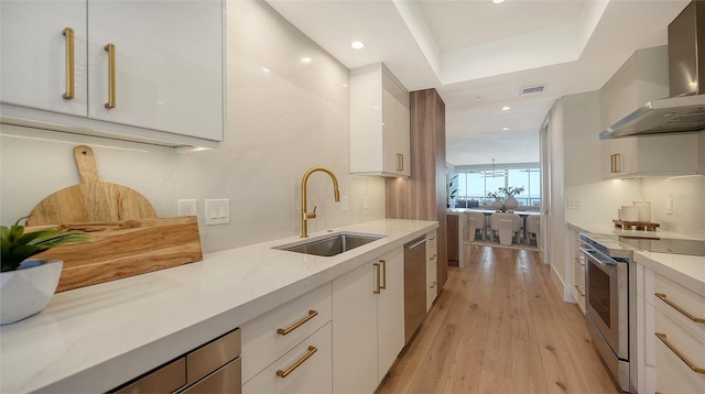 kitchen with wall chimney range hood, sink, appliances with stainless steel finishes, white cabinets, and light stone counters