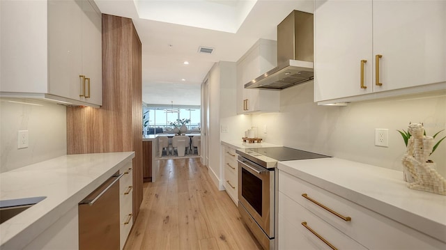 kitchen featuring white cabinets, appliances with stainless steel finishes, and wall chimney exhaust hood