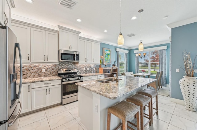 kitchen with sink, light stone counters, an island with sink, pendant lighting, and appliances with stainless steel finishes