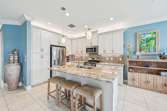 kitchen featuring stainless steel appliances, sink, light stone counters, an island with sink, and pendant lighting